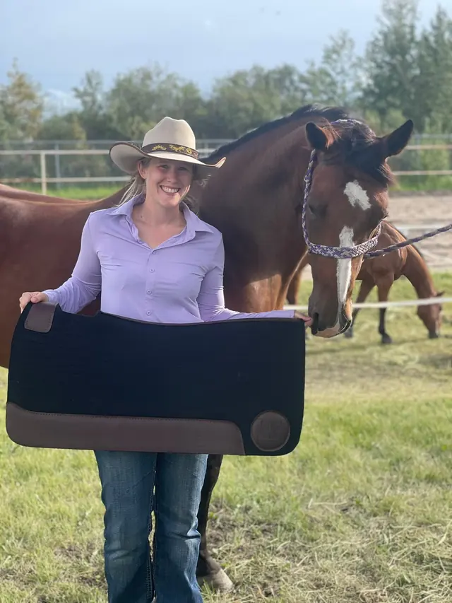 Alyssa standing with Pushy, her bay mare, holding a saddle pad
